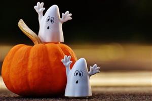 Two little ghosts near a pumpkin.